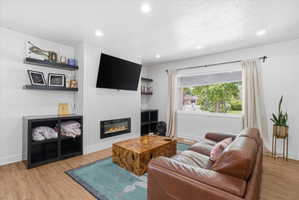 Living area with light wood-style floors, recessed lighting, a glass covered fireplace, and a textured ceiling