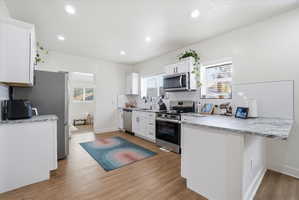 Kitchen featuring a peninsula, backsplash, white cabinetry, stainless steel appliances, and light wood-style flooring