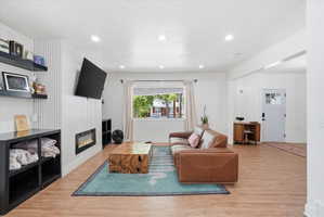 Living area with light wood-style flooring, a textured ceiling, recessed lighting, and a glass covered fireplace
