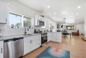 Kitchen featuring white cabinets, stainless steel appliances, light finished floors, a peninsula, and open floor plan