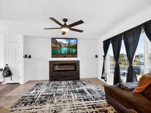 Living room featuring a glass covered fireplace, light wood finished floors, and ceiling fan