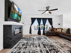 Living room featuring wainscoting, a glass covered fireplace, light wood-type flooring, ceiling fan, and wooden walls