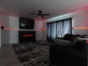 Living room featuring wainscoting, ceiling fan, a glass covered fireplace, wood finished floors, and wooden walls