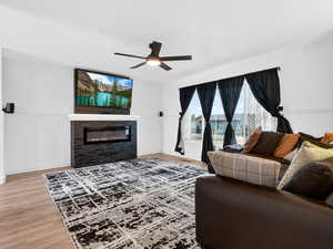 Living room with a wainscoted wall, light wood finished floors, a glass covered fireplace, and a ceiling fan