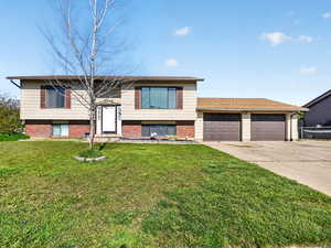 Split foyer home with brick siding, a front lawn, and concrete driveway