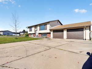 Split foyer home with driveway, brick siding, an attached garage, and a front lawn