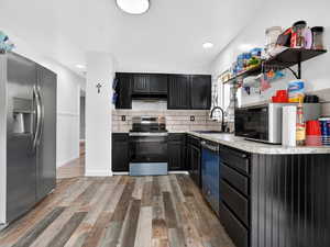 Kitchen featuring light countertops, stainless steel appliances, dark cabinetry, decorative backsplash, and dark wood finished floors