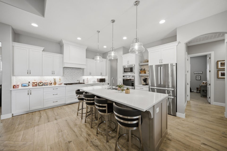Two tone kitchen featuring stainless steel appliances, a center island with sink, a breakfast bar, tasteful backsplash, and pendant lighting