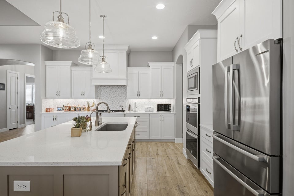 Kitchen featuring stainless steel appliances, arched walkways, light wood-style floors, a center island with sink, and light stone counters