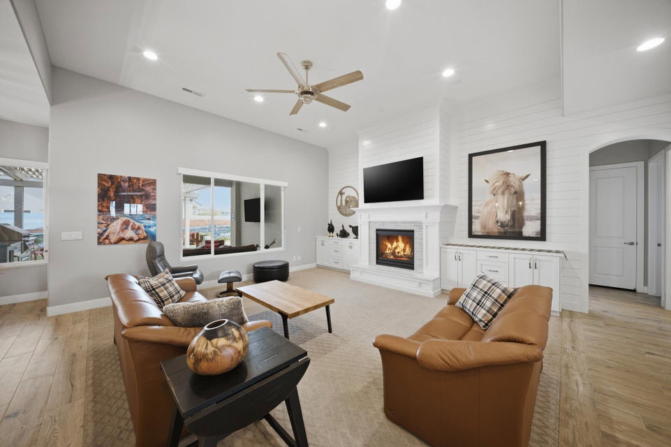 Living room with arched walkways, a glass covered fireplace, light wood-style floors, ceiling fan, and recessed lighting