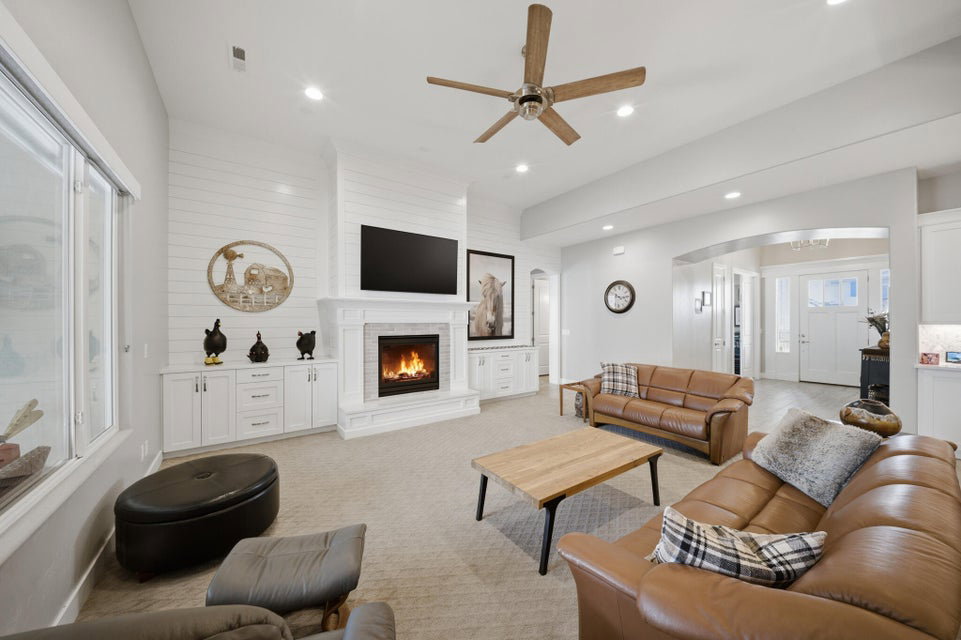 Living area featuring ceiling fan, light colored carpet, a lit fireplace, arched walkways, and recessed lighting