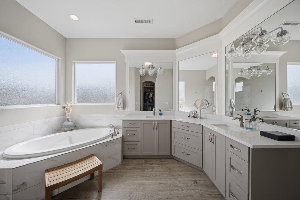 Full bathroom featuring double vanity, healthy amount of natural light, a garden tub, and light wood finished floors