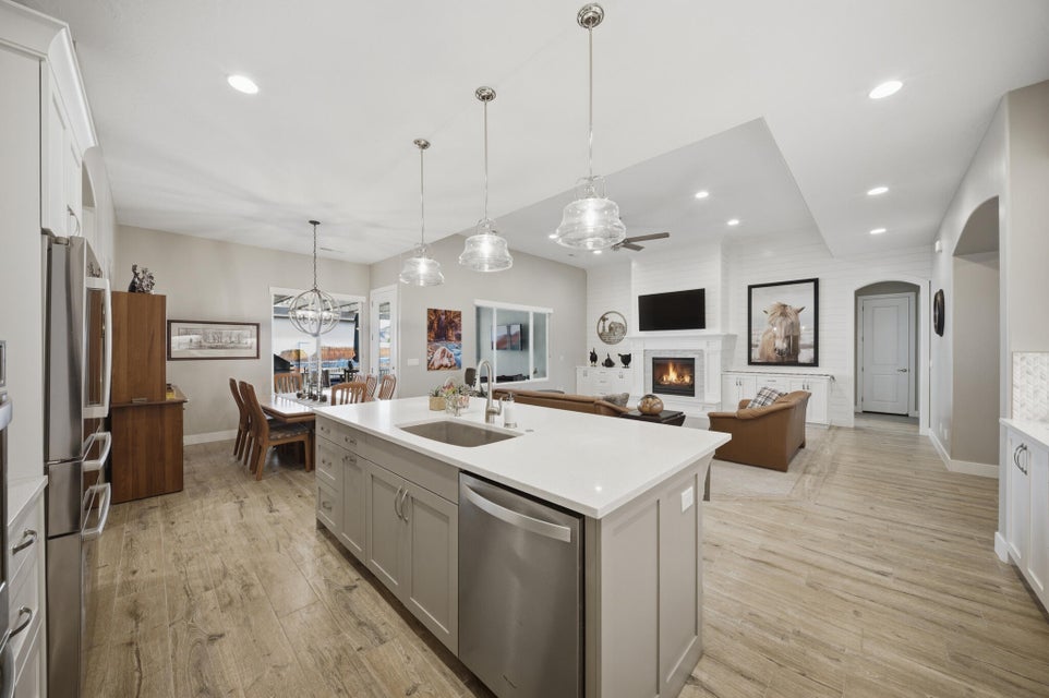 Kitchen featuring a lit fireplace, open floor plan, light wood-style floors, a center island with sink, and stainless steel appliances