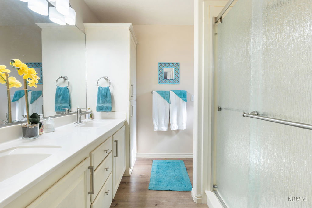 Full bath with double vanity, a stall shower, and light wood finished floors