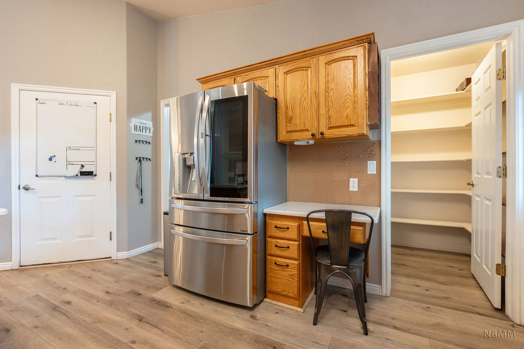 Kitchen featuring stainless steel refrigerator with ice dispenser, wood finish cabinets, light wood-style flooring, and built in desk