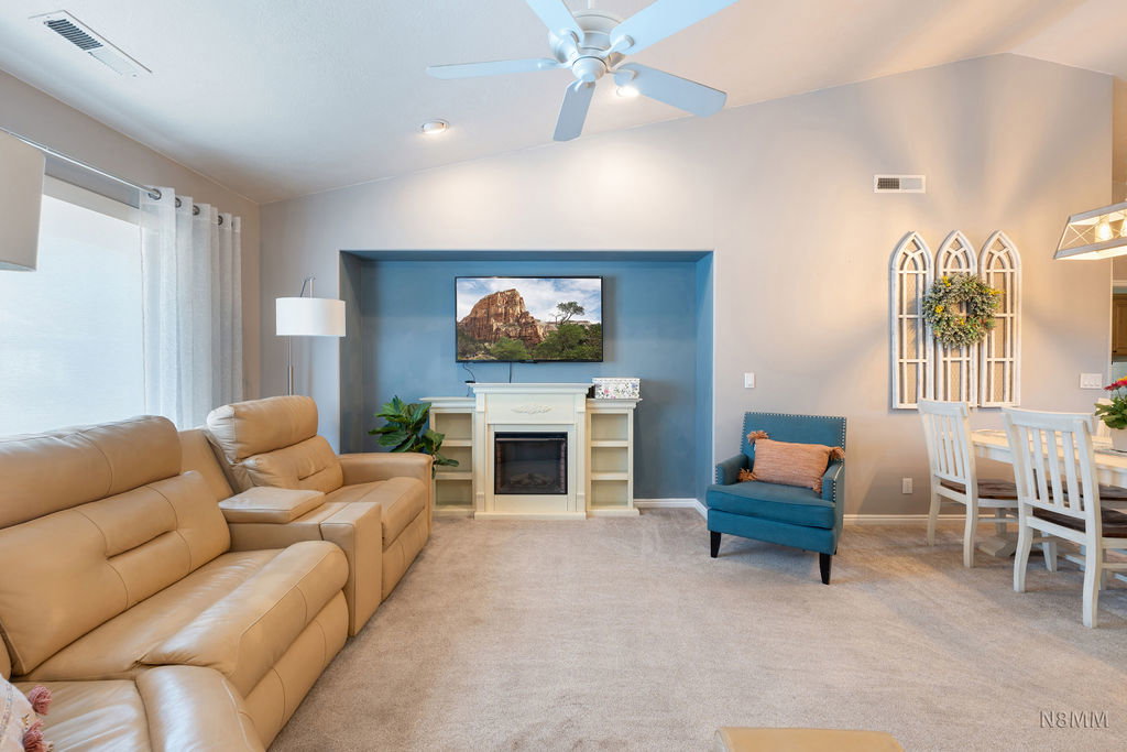 Living area with lofted ceiling, ceiling fan, a glass covered fireplace, and carpet floors