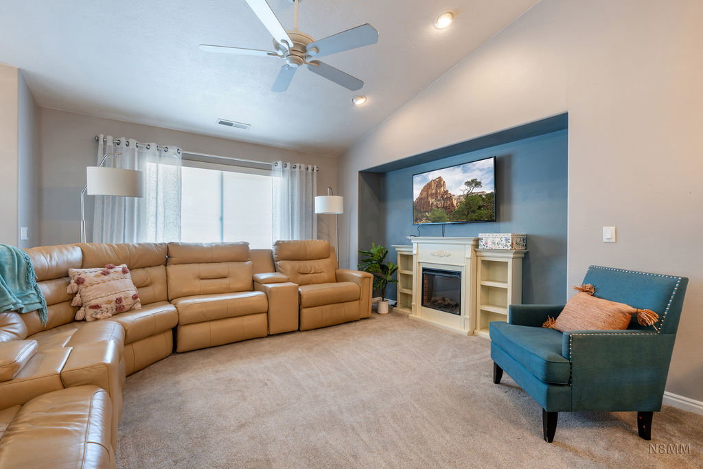 Carpeted living area featuring recessed lighting, a ceiling fan, vaulted ceiling, and a glass covered fireplace