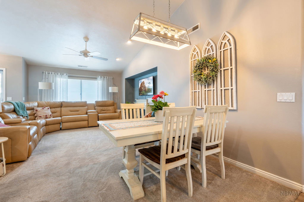 Dining area featuring ceiling fan, light colored carpet, and lofted ceiling