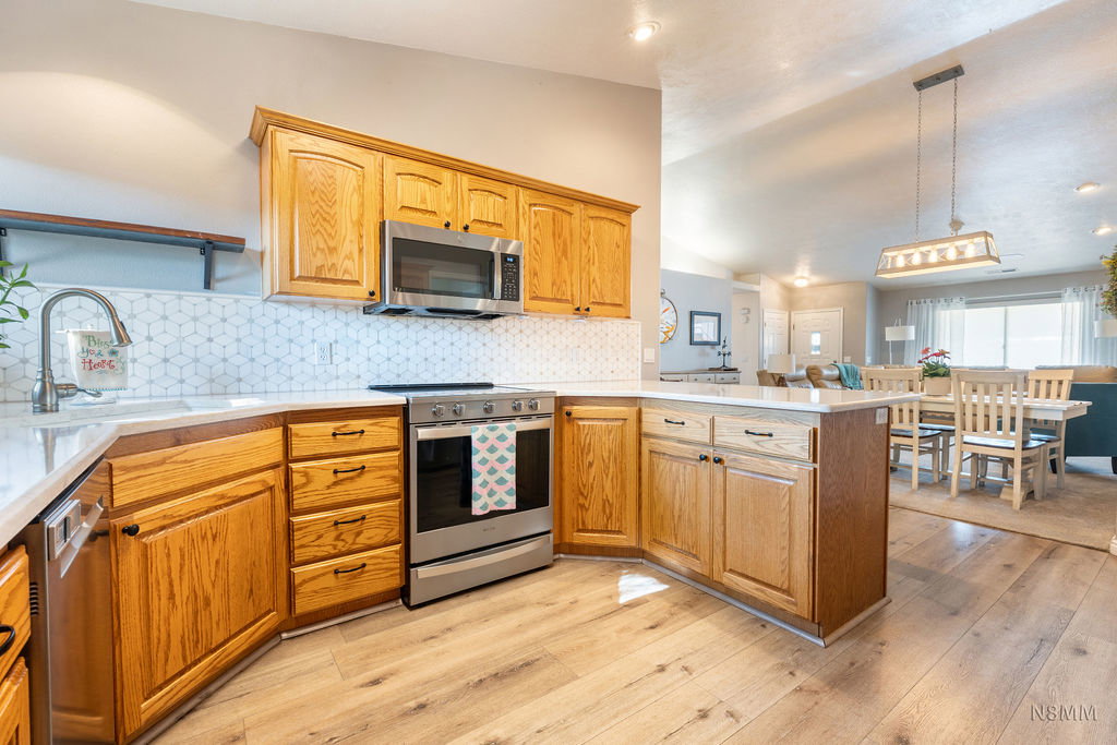 Kitchen featuring stainless steel appliances, light wood-style floors, lofted ceiling, decorative light fixtures, and a peninsula