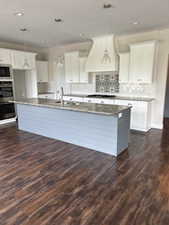 Dual tone kitchen featuring a large island, dark wood-type flooring, decorative light fixtures, dark stone counters, and dual tone cabinets