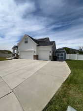 View of side of home featuring concrete driveway, an attached garage, board and batten siding, roof mounted solar panels, and a storage shed