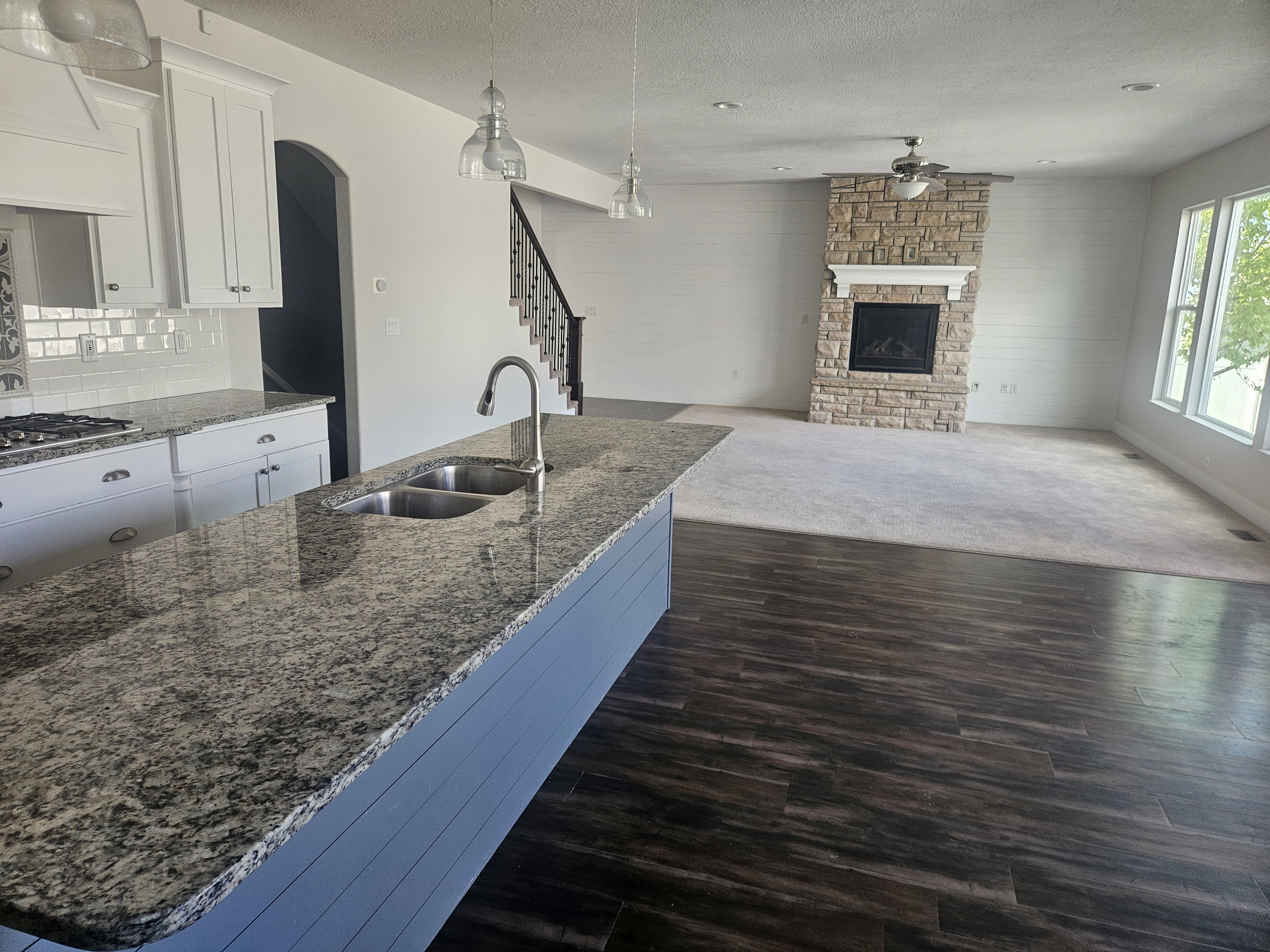 Kitchen with dark stone counters, a textured ceiling, arched walkways, a stone fireplace, and white cabinetry