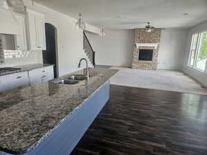 Kitchen with dark stone counters, a textured ceiling, arched walkways, a stone fireplace, and white cabinetry