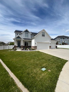 View of front of home featuring board and batten siding, driveway, roof mounted solar panels, and a garage