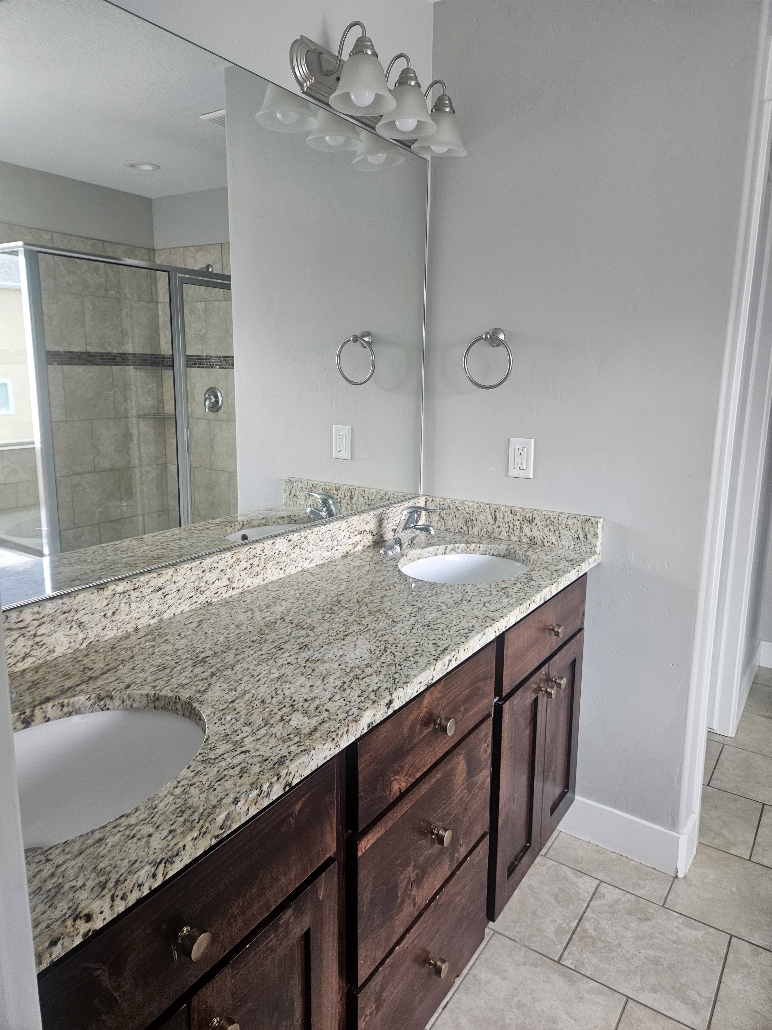 Full bath with double vanity, light tile patterned floors, and a stall shower
