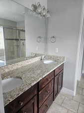 Full bath with double vanity, light tile patterned floors, and a stall shower