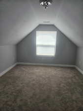Additional living space with dark carpet and a textured ceiling