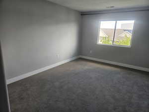 Spare room featuring dark carpet and baseboards