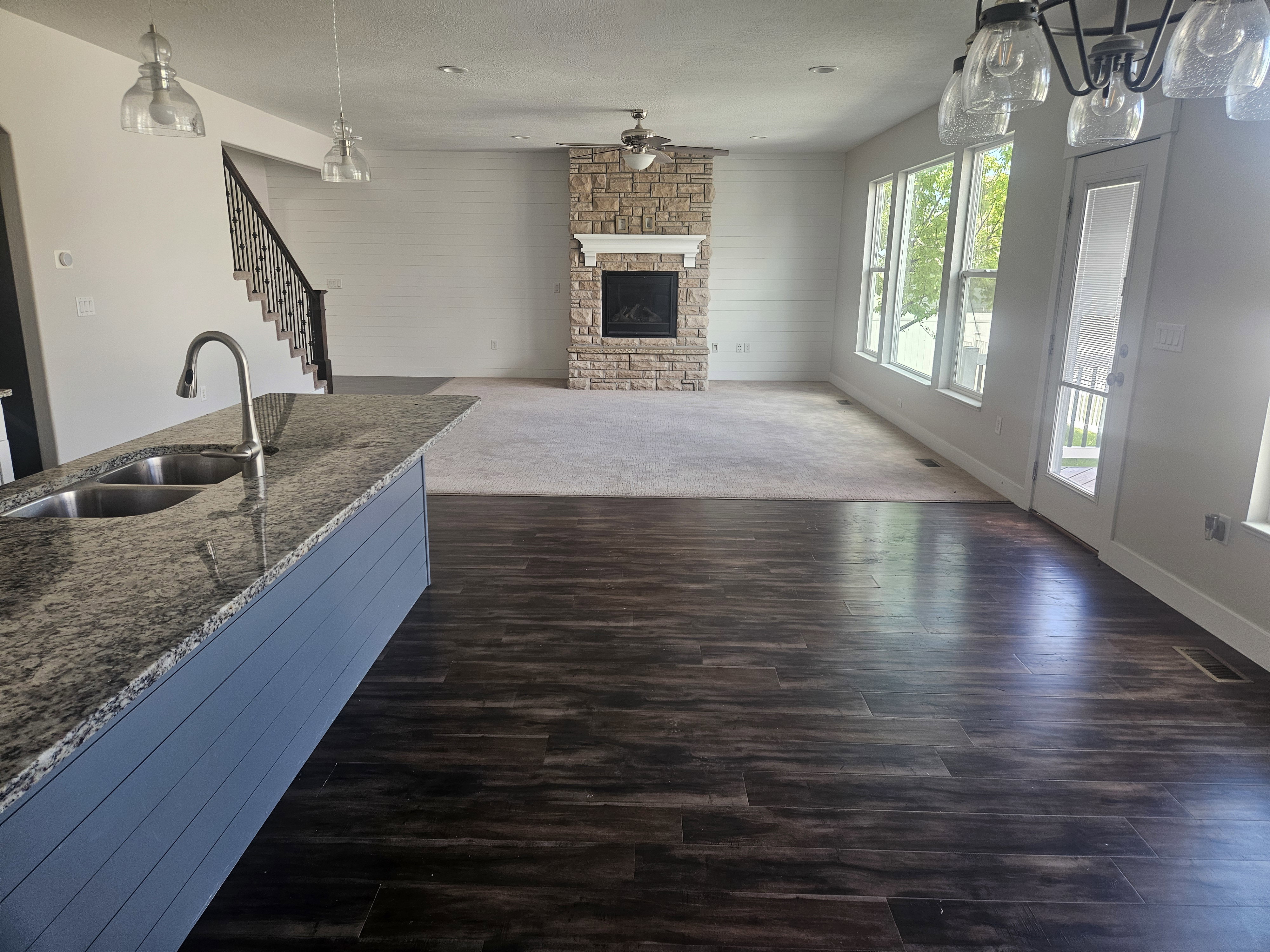 Kitchen featuring pendant lighting, a stone fireplace, dark stone countertops, open floor plan, and dark wood-style flooring