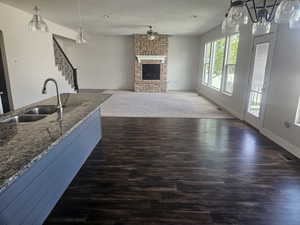 Kitchen featuring pendant lighting, a stone fireplace, dark stone countertops, open floor plan, and dark wood-style flooring