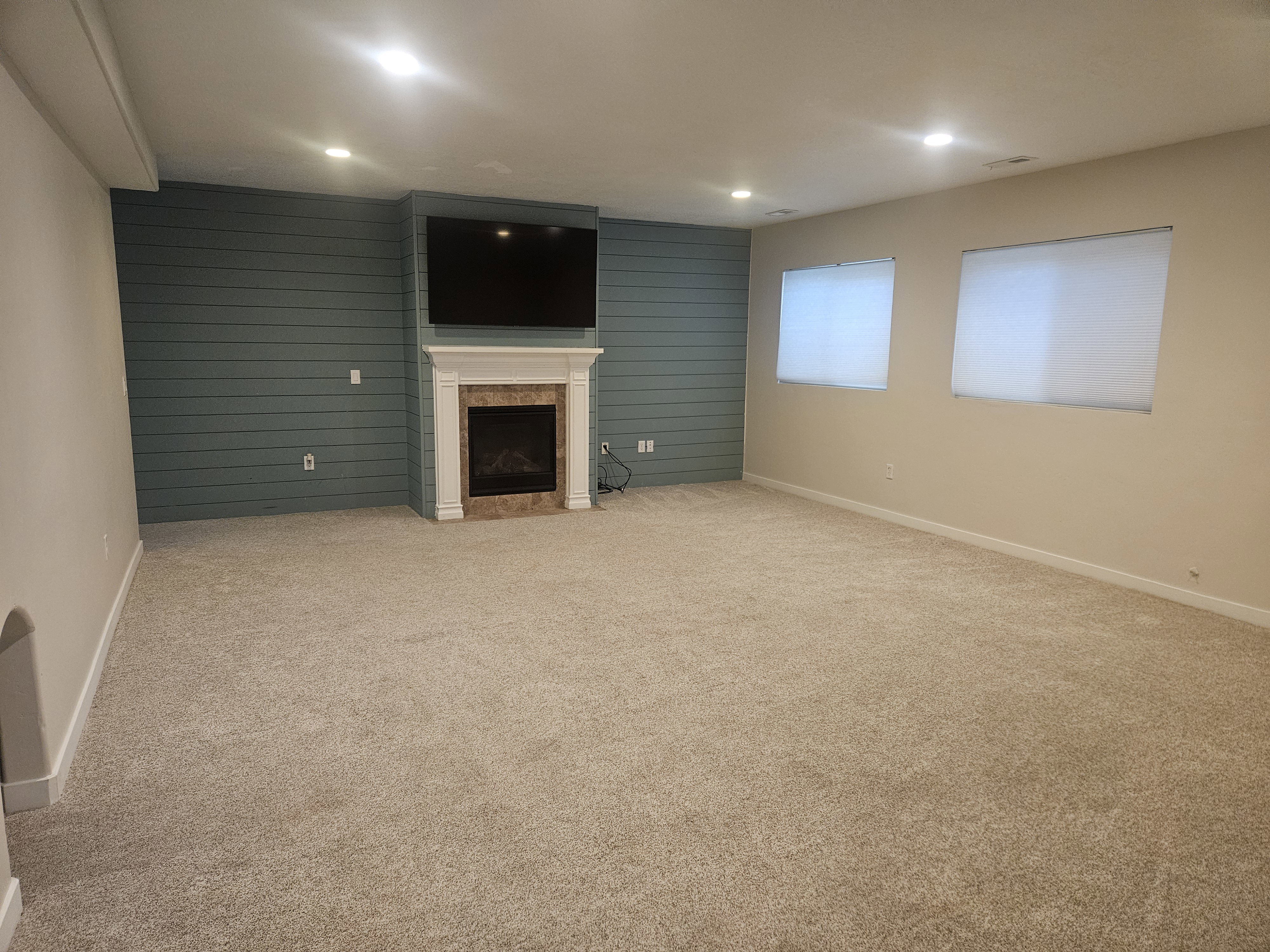 Unfurnished living room featuring an accent wall, light carpet, a fireplace, recessed lighting, and wooden walls