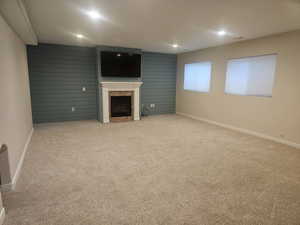 Unfurnished living room featuring an accent wall, light carpet, a fireplace, recessed lighting, and wooden walls