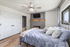 Bedroom featuring wood finished floors, a ceiling fan, a fireplace, a closet, and wooden walls