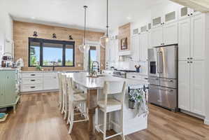 Kitchen featuring white cabinetry, wooden walls, light stone countertops, high end appliances, and a kitchen island with sink