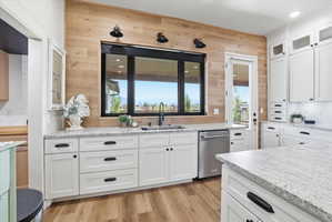 Kitchen featuring white cabinetry, glass insert cabinets, light wood-style floors, light stone counters, and stainless steel dishwasher