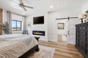 Bedroom featuring a barn door, light wood-style flooring, a large fireplace, a ceiling fan, and wood ceiling