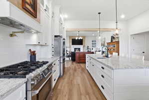 Two tone kitchen with premium appliances, a fireplace, light stone counters, two tone cabinets, and light wood finished floors