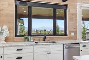 Kitchen with a mountain view, light stone countertops, dishwasher, and white cabinets