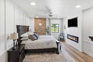 Bedroom featuring a large fireplace, a decorative wall, light wood-type flooring, ceiling fan, and recessed lighting