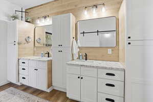 Bathroom with wood walls, two vanities, and dark wood-type flooring