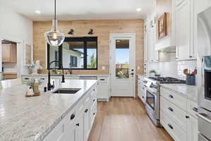 Kitchen featuring stainless steel appliances, hanging light fixtures, white cabinetry, light wood-style floors, and light stone counters