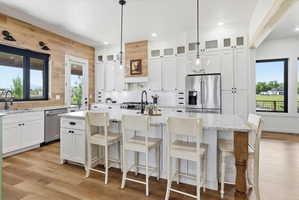 Kitchen with white cabinetry, stainless steel appliances, light wood-style floors, and light stone counters