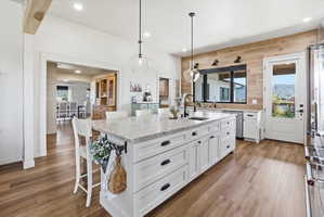Kitchen featuring white cabinetry, light stone countertops, wood walls, an island with sink, and light wood-style flooring