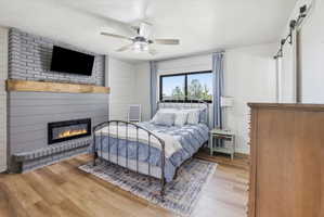 Bedroom featuring a barn door, light wood-style floors, a ceiling fan, a textured ceiling, and wooden walls