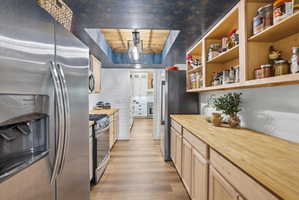 Kitchen featuring wooden counters, stainless steel appliances, light wood finish cabinetry, light wood finished floors, and a wooden tray ceiling