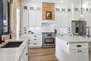Kitchen with white cabinetry, high quality appliances, light wood finished floors, light stone counters, and decorative backsplash